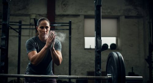 Ein Athlet kreidet seine Hände ein, im Hintergrund eine Hantel für den 5x5 Trainingsplan. Ein Athlet kreidet seine Hände ein, im Hintergrund eine Hantel für den 5x5 Trainingsplan.