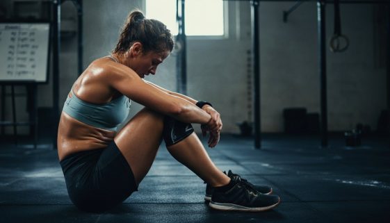 Eine erschöpfte Athletin sitzt nach einem der anspruchsvollen Benchmark WODs auf dem Boden einer Fitness-Box.