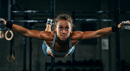 Eine Athletin in einer CrossFit-Box führt mit voller Konzentration einen Butterfly Pull-up aus. Eine Athletin in einer CrossFit-Box führt mit voller Konzentration einen Butterfly Pull-up aus.