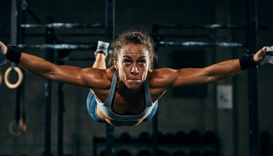 Eine Athletin in einer CrossFit-Box führt mit voller Konzentration einen Butterfly Pull-up aus.