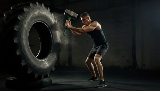 Ein Kampfsportler macht explosives Crosstraining mit einem Vorschlaghammer auf einem Reifen.