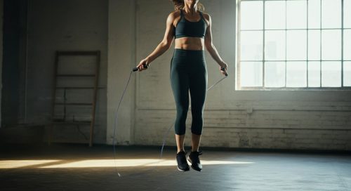 Eine Athletin in einer minimalistischen Halle konzentriert sich beim Double Unders lernen. Eine Athletin in einer minimalistischen Halle konzentriert sich beim Double Unders lernen.