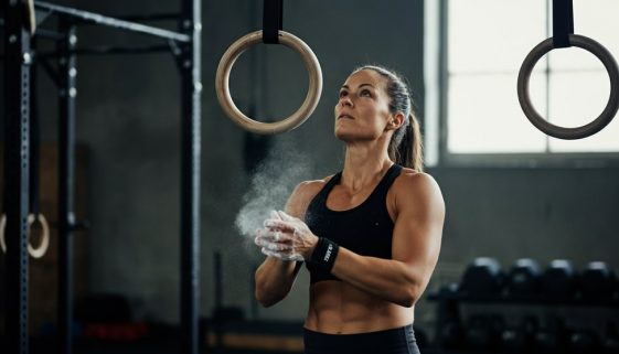 Eine Athletin kreidet ihre Hände ein und blickt konzentriert auf Turnringe für ihr Gymnastics Crosstraining.