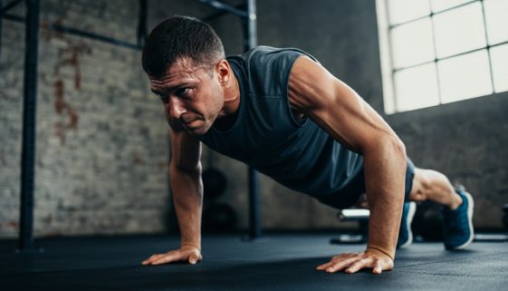 Ein Athlet in der anstrengendsten Phase einer Handstand Push Up Progression an einer Ziegelsteinwand, hochkonzentriert.