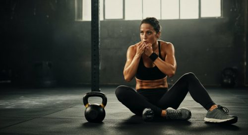 Erschöpfte, aber zufriedene Frau nach einem intensiven HIIT mit Kettlebell in einem minimalistischen Gym.
