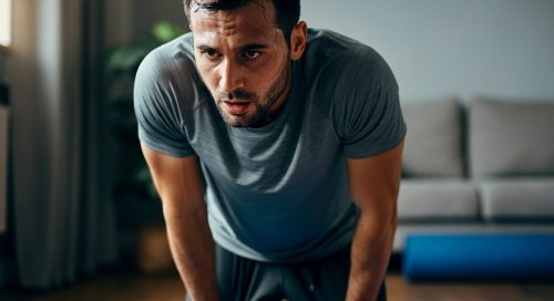 Mann macht eine Pause bei seinem intensiven HIIT Oberkörper Workout zuhause und stützt sich erschöpft ab. Mann macht eine Pause bei seinem intensiven HIIT Oberkörper Workout zuhause und stützt sich erschöpft ab.