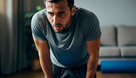 Mann macht eine Pause bei seinem intensiven HIIT Oberkörper Workout zuhause und stützt sich erschöpft ab.