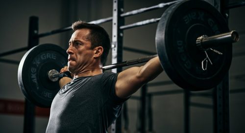 Ein fokussierter Athlet führt einen anspruchsvollen Langhantel Komplex in einem Gym aus.