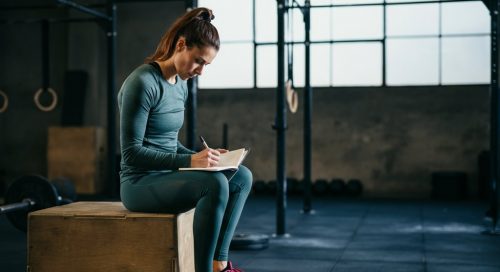 Fokussierte Athletin plant ihre Makros für CrossTraining in einem Notizbuch in der Box.