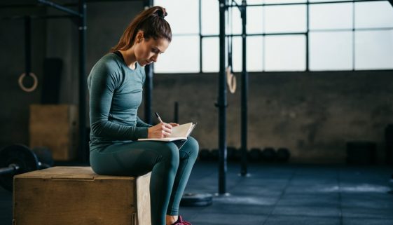 Fokussierte Athletin plant ihre Makros für CrossTraining in einem Notizbuch in der Box.