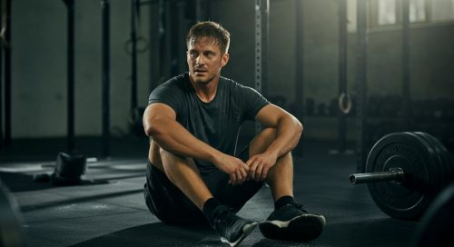 Erschöpfte Athletin sitzt auf dem Gym-Boden als Sinnbild für starken Muskelkater nach einem WOD. Erschöpfte Athletin sitzt auf dem Gym-Boden als Sinnbild für starken Muskelkater nach einem WOD.