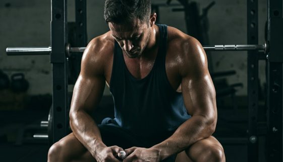 Ein athletischer Mann pausiert nach dem Training gemäß seinem Powerbuilding Trainingsplan in einem Gym.