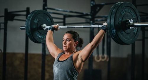 Eine Athletin hält nach dem Snatch lernen eine Hantel mit perfekter Technik über dem Kopf. Eine Athletin hält nach dem Snatch lernen eine Hantel mit perfekter Technik über dem Kopf.
