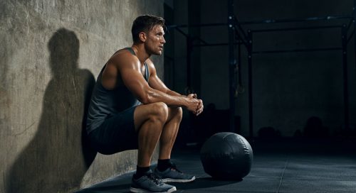 Erschöpfter Athlet lehnt nach dem Training an der Wand, was die Wichtigkeit der Wall Balls Technik zeigt.